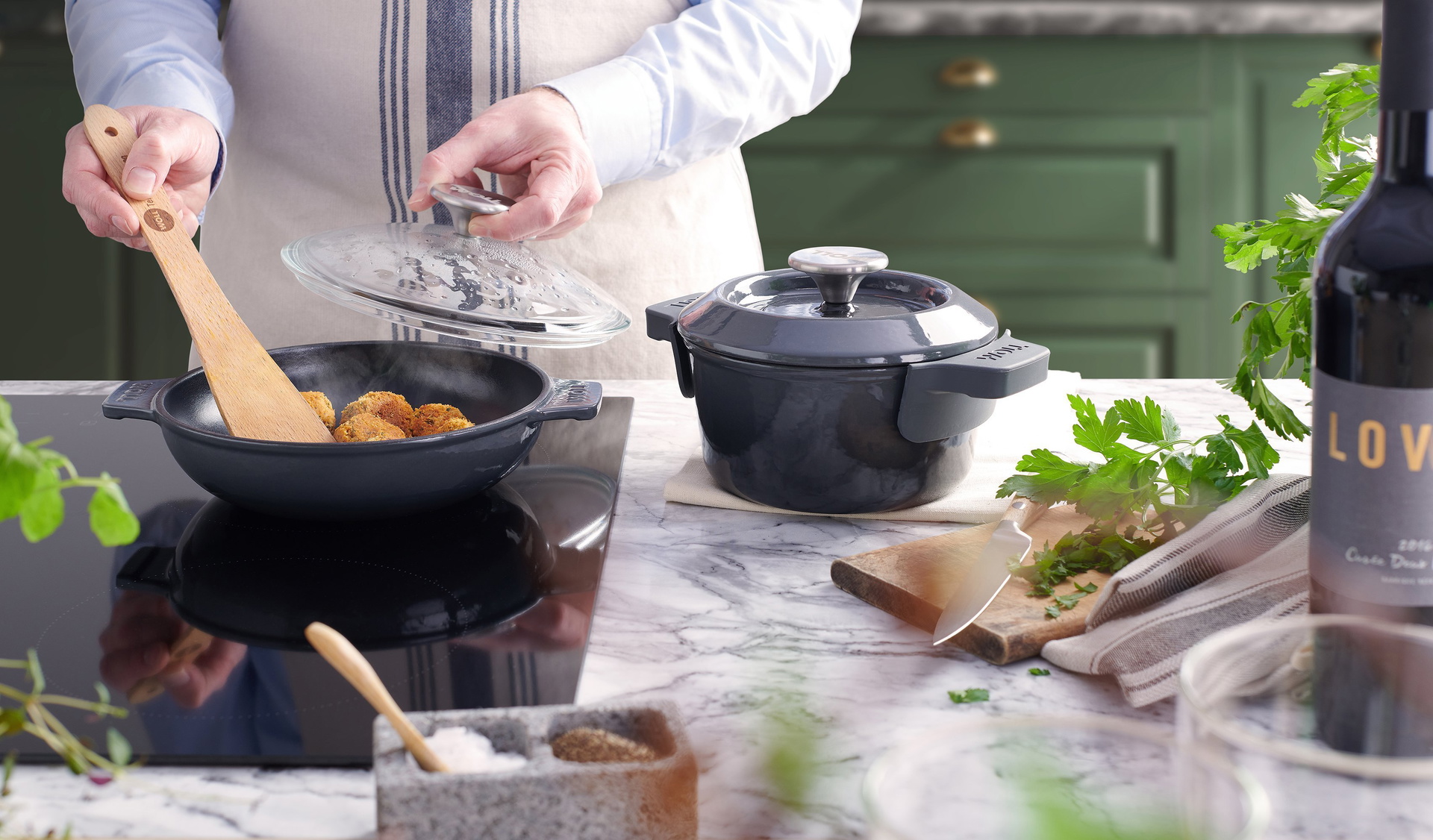 5520CI-030-116CI-030_Turn_2000x3400px_RGB_Web Auf dem Herd steht eine graue, runde Iron Servierpfanne, in der Falafel angebraten werden. Daneben steht ein Iron Topf mit Deckel.