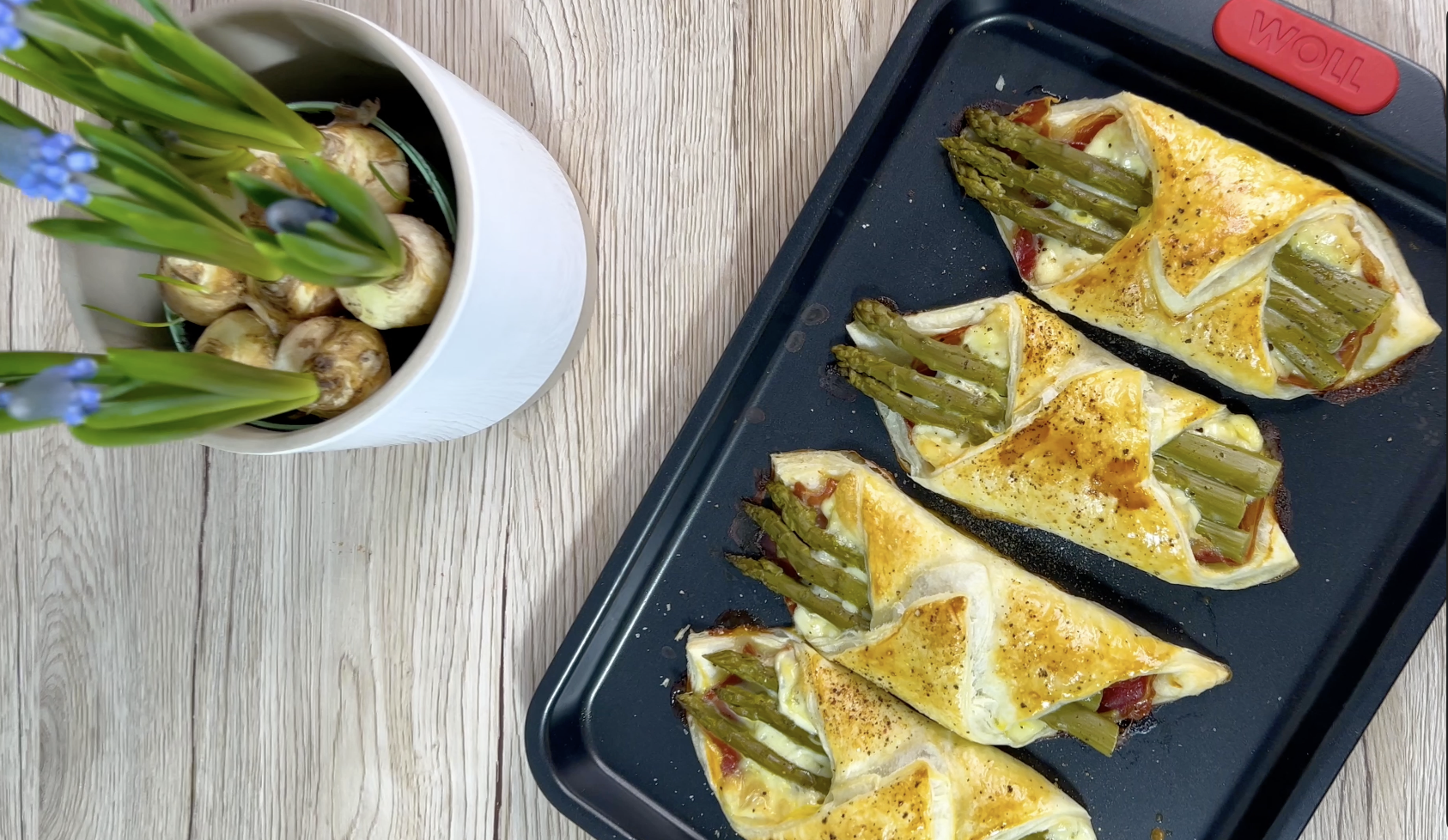 Auf einem Tisch steht ein Backblech der Serie Let's Bake!, auf dem frisch gebackene Spargeltaschen liegen. Daneben steht eine Topfpflanze.