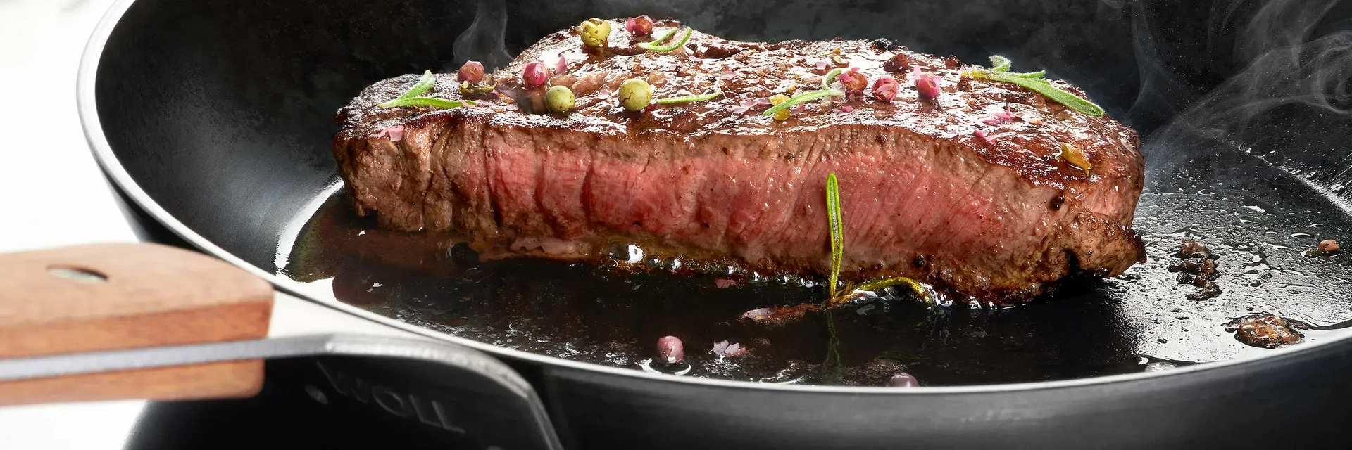 In einer runden, heißen Pfanne der Serie Carbon Steel mit festem Holzstiel wird ein Stück Fleisch scharf angebraten.