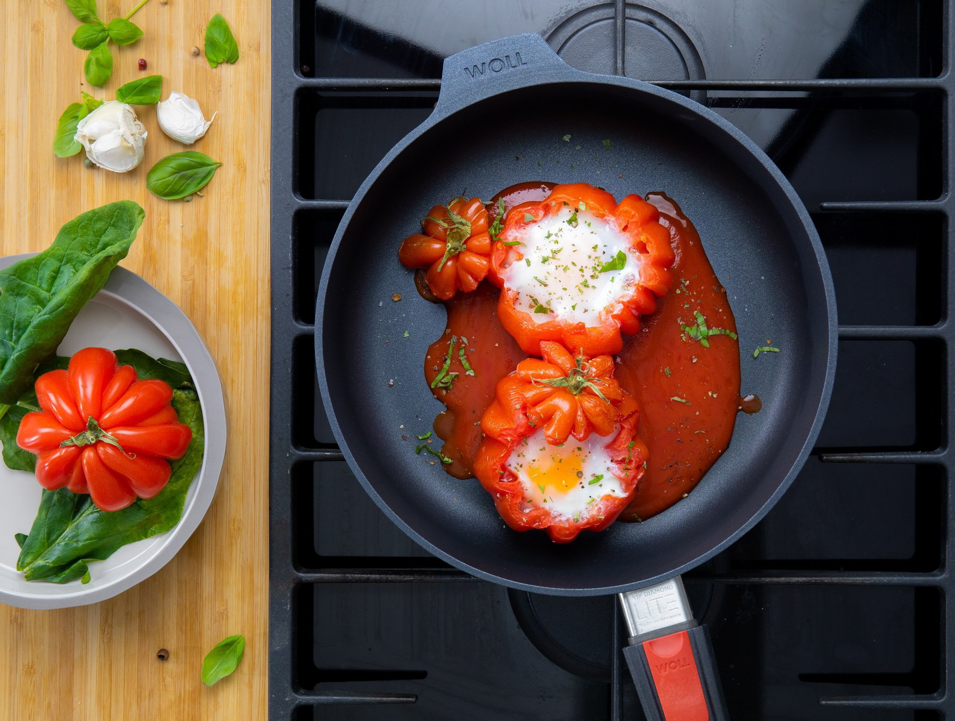 Auf dem Herd steht eine runde, heiße Diamond Ltie Pfanne mit abnehmbarem Stiel. In dieser befindet sich gefüllte Tomate mit Ei. Auf der Arbeitsplatte daneben stehen weitere Zutaten.