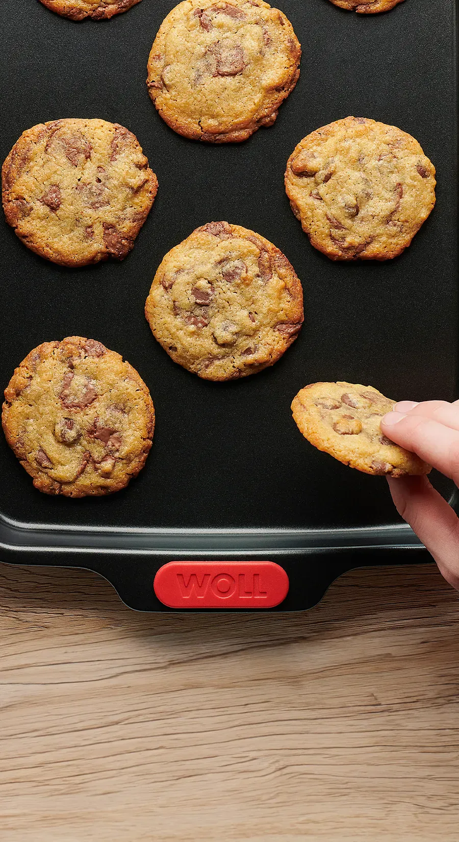 Auf einem rechteckigen Backblech der Serie „Let's Bake!” liegen frisch gebackene Cookies mit Schokoladestückchen. Ein Cookie wird vom Blech genommen.
