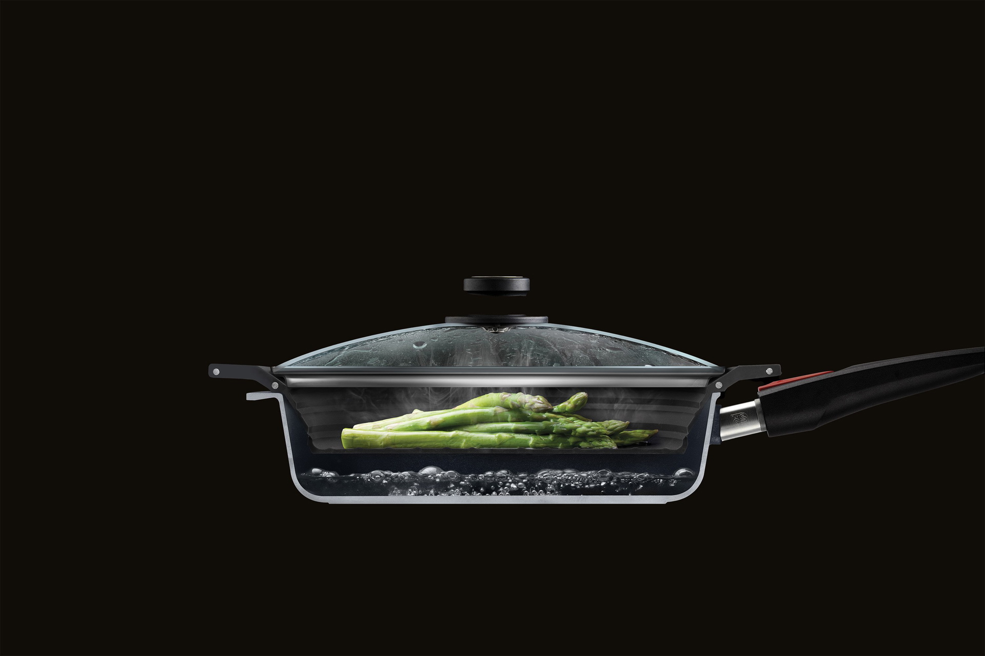 SI24F_steamer Im Querschnitt ist eine halbierte Pfanne mit Glasdeckel zu sehen, in der grüner Spargel mit dem Steam it multifunktionalen Silikoneinsatz gedämpft wird.