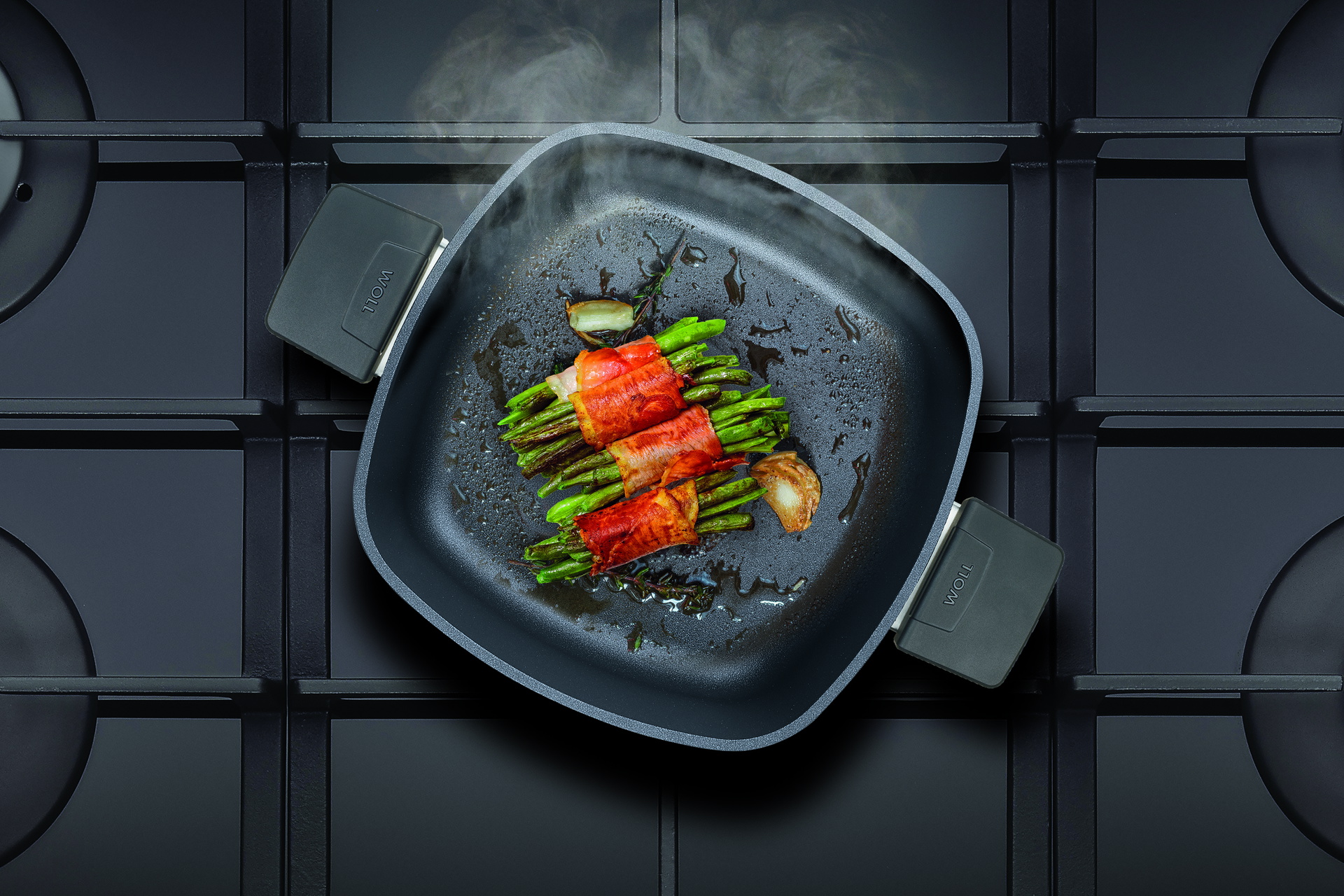 Auf dem Herd steht eine viereckige, heiße Diamond-Lite-Kasserolle ohne Deckel. In dieser werden Bohnen im Speckmantel angebraten.